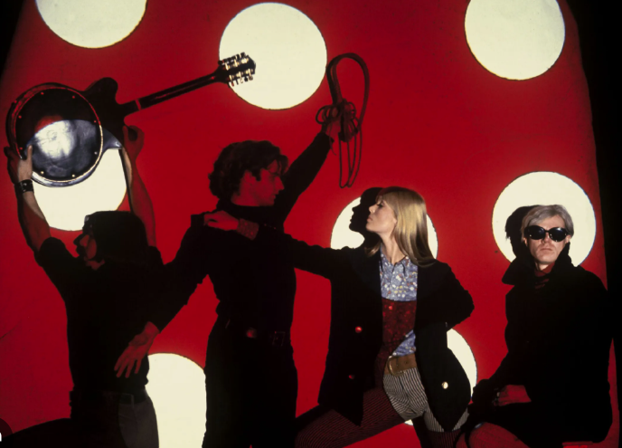 The Velvet Underground with Nico and Andy Warhol posed before a red screen with white circles